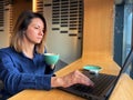 Caucasian woman working online texting on laptop while sitting in cafe with cup of coffee. Female professional typing on Royalty Free Stock Photo