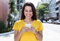 Caucasian woman in yellow shirt sending message with phone in city Royalty Free Stock Photo