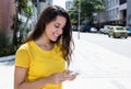 Caucasian woman in yellow shirt typing message at phone in city Royalty Free Stock Photo