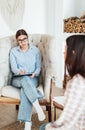 Caucasian woman psychologist in eyeglasses sitting in a chair at the workplace, listens to the patient and takes notes