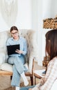 Caucasian woman psychologist in eyeglasses sitting in a chair at the workplace, listens to the patient and takes notes