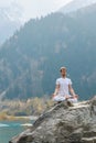 Caucasian yoga man in outdoor meditation sitting on lonely rock island of mountain lake