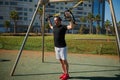 Young adult sportsman doing bodyweight exercises on arms, push ups with suspension straps in urban sports ground