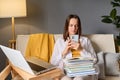 Caucasian young adult woman sitting at home in living room surrounded with educational material laptop and books using mobile Royalty Free Stock Photo