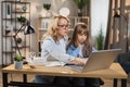 Caucasian young blond woman mother help her beautiful daughter to do homework using laptop Royalty Free Stock Photo