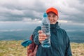 Caucasian young blonde girl shows water from plastic bottle. mountain background.