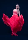 Young Blonde With a Red Silky Dress, That is Flying,  Looking Down, on Deep Blue Background. Fashion Position Royalty Free Stock Photo