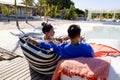 Caucasian young couple enjoying beer and relaxing on cozy loungers at poolside at tourist resort