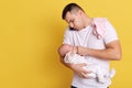 Caucasian young father holding newborn baby in hid hands, calming down little kid, giving nipple, talking phone while taking care Royalty Free Stock Photo