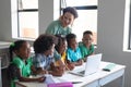 Caucasian young female teacher looking at african american elementary students while teaching laptop Royalty Free Stock Photo