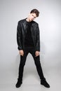 Caucasian young guy posing in studio, full-length portrait of a model in black clothes. Handsome teenager in a black jacket, jeans Royalty Free Stock Photo