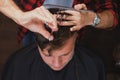 Caucasian young man in Barbershop. Barber is cuttinhg his hair in hipster style.