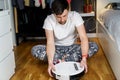 Caucasian young man in christmas pajamas doing vacuum cleaner robot maintenance. Male in winter patterned sleepwear and red socks Royalty Free Stock Photo