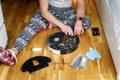 Caucasian young man in christmas pajamas doing vacuum cleaner robot maintenance. Male in winter patterned sleepwear and red socks Royalty Free Stock Photo