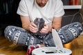 Caucasian young man in christmas pajamas doing vacuum cleaner robot maintenance. Male in winter patterned sleepwear and red socks Royalty Free Stock Photo