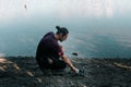 caucasian young man crouching operating drone lying on ground on stony shore of calm crystal clear lake, new zealand Royalty Free Stock Photo