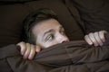 Caucasian young man hiding in bed under the blanket at home. Royalty Free Stock Photo