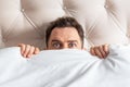 Caucasian young man hiding in bed under the blanket at home Royalty Free Stock Photo