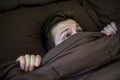 Caucasian young man hiding in bed under the blanket at home. Royalty Free Stock Photo