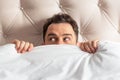 Caucasian young man hiding in bed under the blanket at home Royalty Free Stock Photo