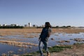 caucasian young man with long hair imitating a guitarist standing near a flooded field near the city