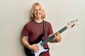 Caucasian young man with long hair playing electric guitar sticking tongue out happy with funny expression Royalty Free Stock Photo