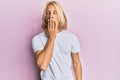 Caucasian young man with long hair wearing casual white t shirt bored yawning tired covering mouth with hand