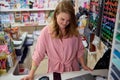 Caucasian young pleasant smiling woman manager standing at a counter with computer in the school stationery store Royalty Free Stock Photo