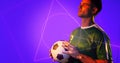 Caucasian young soccer player holding ball by geometric neon design over blue background, copy space