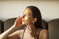 Caucasian young woman applying moisturizing or peeling golden facial mask and touch her face with hands. Side view. Royalty Free Stock Photo