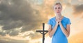 Caucasian young woman with closed eyes praying while standing against silhouette cross during sunset Royalty Free Stock Photo