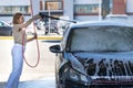 Caucasian young woman driver washing at manual car washing, cleaning with foam, pressured water. Self-service car wash with high-p Royalty Free Stock Photo