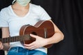 Caucasian young woman playing ukulele and wearing face mask. Black background with copy space