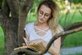 Caucasian young woman reading a book in the park leaning on a tree branch Royalty Free Stock Photo