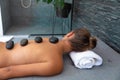 Caucasian young woman receiving hot stone massage lying on the massage table