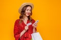 Caucasian young woman in red summer dress with straw hat smiling and holding credit card, mobile phone, and shopping Royalty Free Stock Photo