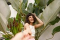 Caucasian young woman smiling looking at camera holding photographer& x27;s hand on background of plants. Royalty Free Stock Photo