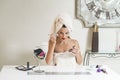 Young woman with a towel on her head painting her lips in front of a mirror