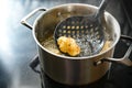 Cauliflower floret on a spatula deep fried in a pot with steaming cooking oil on the stove, creative preparation of a vegetable