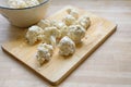 Cauliflower pieces coated with spicy batter on a wooden cutting board as preparation for frying, vegetarian cooking with