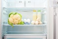 Cauliflower, white eggs, champignon mushrooms and two glass bottles of yoghurt on shelf of open empty refrigerator Royalty Free Stock Photo