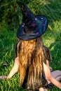 Causcasian blond girl with long hair in halloween witch costume sitting on a green grass Royalty Free Stock Photo
