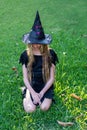 Causcasian blond girl with long hair in halloween witch costume sitting on a grass Royalty Free Stock Photo