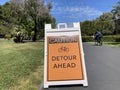 Caution. Detour ahead warning sign with bicycle emblem. Bicyclist is passing by