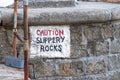 Caution Slippery Rocks sign painted on to a wall at the coast Royalty Free Stock Photo