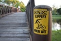 Caution Slippery When Wet Warning Sign with Bike Rider On Bridge Royalty Free Stock Photo