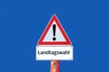 Caution warning sign state election on blue background in german