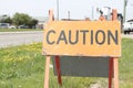 caution word caption text sandwich board wooden sign next to sidewalk and grass. p