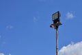 A CCTV camera and a square spotlight are mounted on a metal pole against the blue sky. Organized video surveillance syste Royalty Free Stock Photo