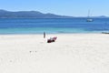 Beach with white sand, chairs and beach umbrella. Bay with turquoise water and sailing boat. Cee, A Coruna Province, Spain. Royalty Free Stock Photo